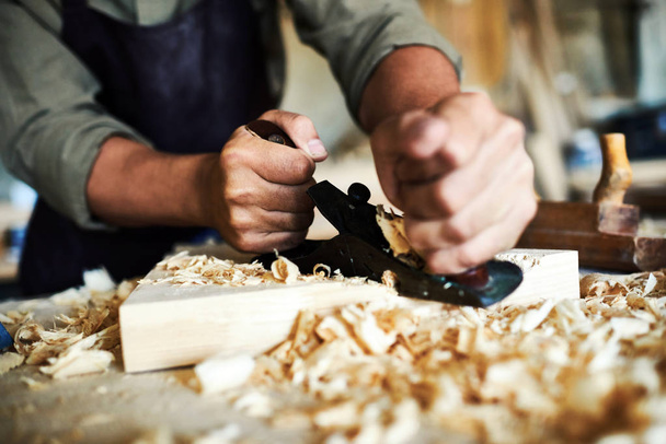 Closeup portret van sterke mannelijke handen scheren stuk hout met het gereedschap vlak in timmerlieden werkplaats maken van meubels - Foto, afbeelding