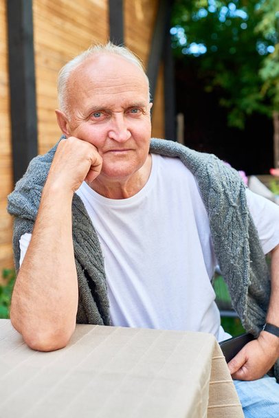 Pasa do portret przystojny mężczyzna starszy patrząc na kamery z głęboko niebieskie oczy siedząc przy stoliku w kawiarni na świeżym powietrzu i czeka na jego zamówienie. - Zdjęcie, obraz
