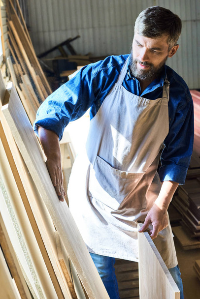 Πορτρέτο του ειδικευμένου ξυλουργού αγγίζοντας απαλά λεία κομμάτι του ξύλου σε ξυλουργικές εργασίες αποθήκευσης, επιλέγοντας τα καλύτερα υλικά - Φωτογραφία, εικόνα