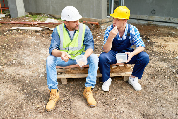 Kahden rakennustyöntekijän muotokuva tauolla paikan päällä syömässä lounasta ulkona olevista muoviastioista
 - Valokuva, kuva