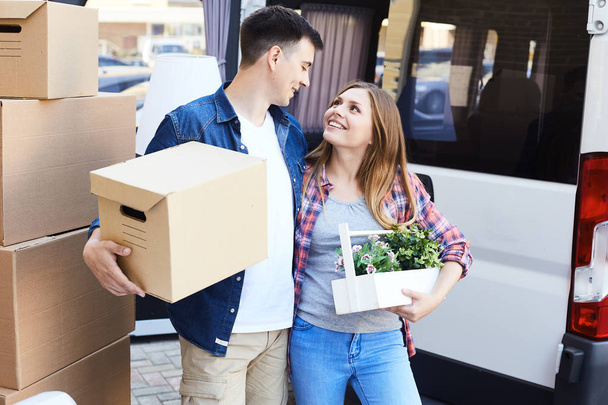 Portrait of happy young couple embracing  looking at each other tenderly while loading cardboard boxes to moving van outdoors - 写真・画像