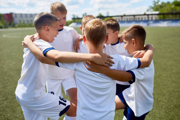 Equipo de chicos en uniforme de fútbol abrazando sonriendo felizmente durante la práctica
 - Foto, imagen
