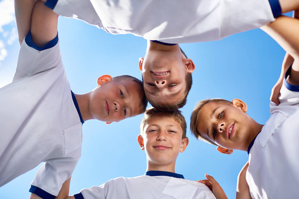 Low angle portrait of junior football team standing in circle and smiling  at camera against blue sky - Foto, Imagen