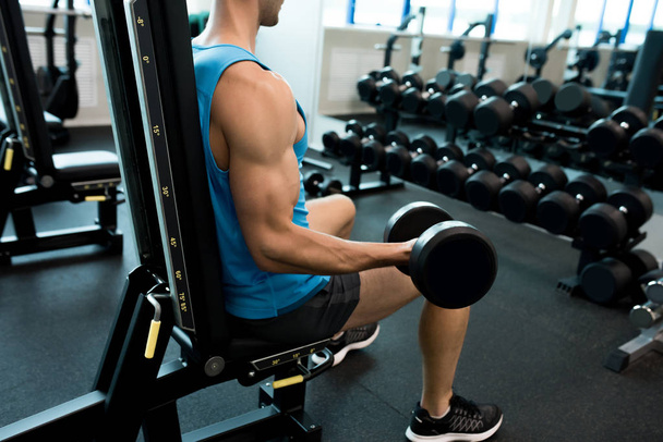 Visão lateral retrato de homem bonito jovem levantando dumbbell bombeamento músculos do braço durante o treinamento de força no ginásio moderno
 - Foto, Imagem