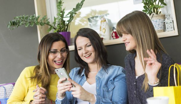 Freunde unterhalten sich und benutzen ein Mobiltelefon / drei Mädchen sitzen in einem Café und beobachten das Geschehen in sozialen Netzwerken - Foto, Bild