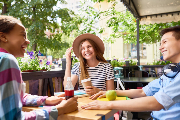 Gruppe junger Leute plaudert beim Mittagessen im Café im Freien an einem sonnigen Sommertag, alle lachen und lächeln - Foto, Bild