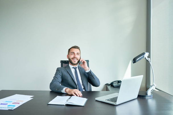 Ritratto di imprenditore di successo seduto alla grande scrivania nell'ufficio moderno che parla per telefono e ride, copia lo spazio
 - Foto, immagini