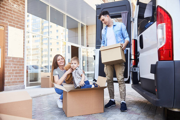 Portrait de jeune famille heureuse avec un petit garçon chargeant des boîtes en carton dans une camionnette en mouvement à l'extérieur
 - Photo, image