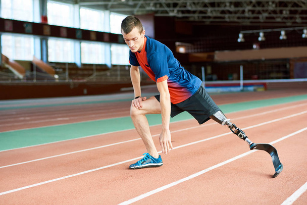 Ολόσωμο πορτρέτο ανάπηροι νεαρό αθλητή του πλανήτη μέχρι πριν από την εκτέλεση πράξη στο σύγχρονο γυμναστήριο τεντώνοντας τα πόδια στο δρόμο - Φωτογραφία, εικόνα