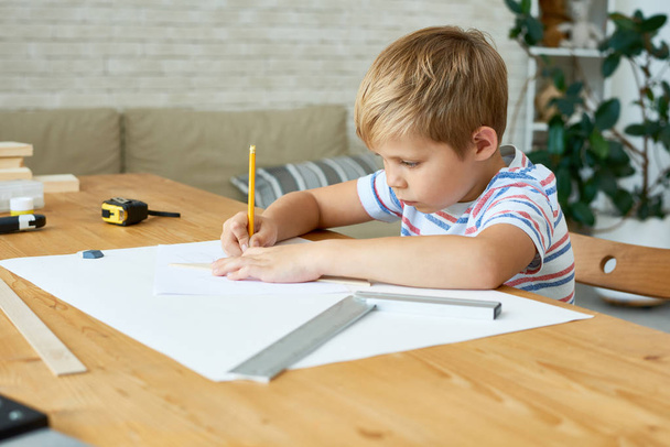 Портрет милого маленького мальчика, который пишет или рисует аккуратно сидя за столом и делает домашнюю работу, копирует пространство
 - Фото, изображение
