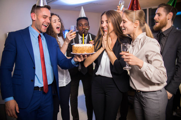 ケーキとシャンパンのオフィスで同僚の誕生日を祝う陽気な若い労働者 - 写真・画像