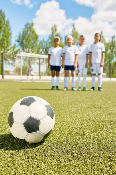 Primer plano de la pelota de fútbol acostado sobre hierba verde con el equipo en el fondo
 - Foto, Imagen