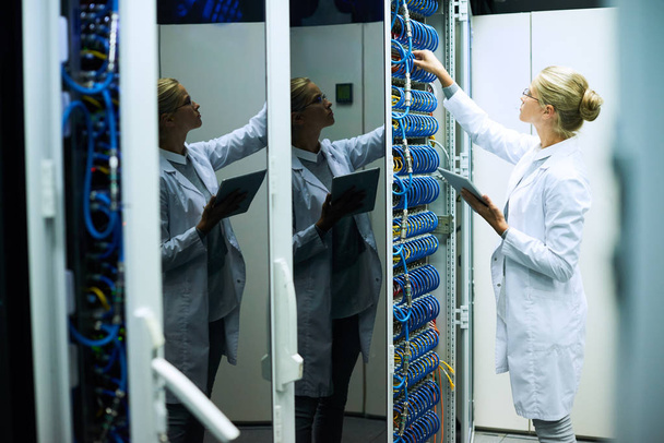 Jonge vrouw dragen laboratoriumjas werken met servercluster in supercomputer onderzoekscentrum - Foto, afbeelding