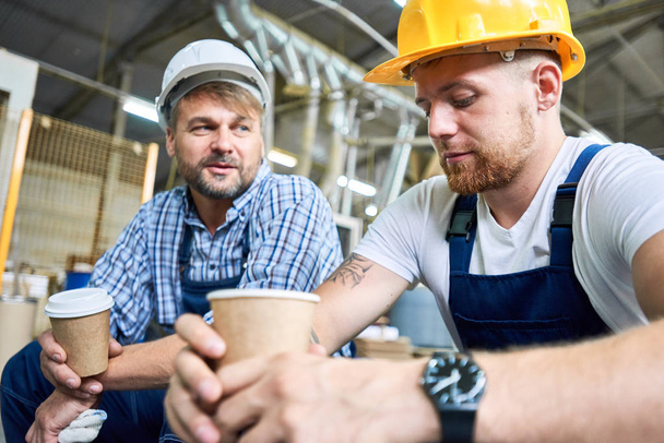 Muotokuva kahdesta työntekijästä, jotka pitävät kypärää, taukoa töistä, juovat kahvia ja lepäävät rakennustyömaalla.
 - Valokuva, kuva