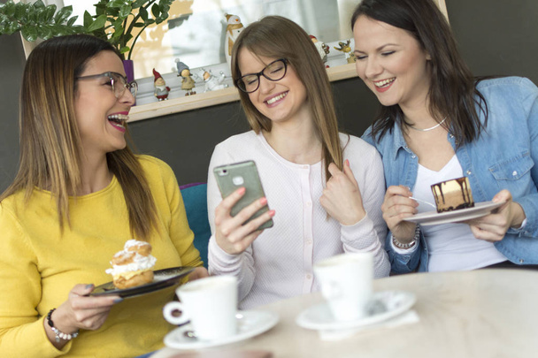 Een volwassen meisje toont haar vrienden dat een foto van haar nieuwe vriendje op een smartphone/een mooi lachende meisje toont een foto van haar nieuwe vriendje aan haar vrienden - Foto, afbeelding