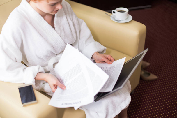 High angle portrait of young businesswoman dressed in bathrobe working with laptop and documents in hotel room during business travel, copy space - Photo, Image