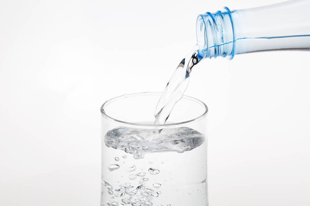 Despejar água da garrafa em vidro sobre fundo branco. - Foto, Imagem