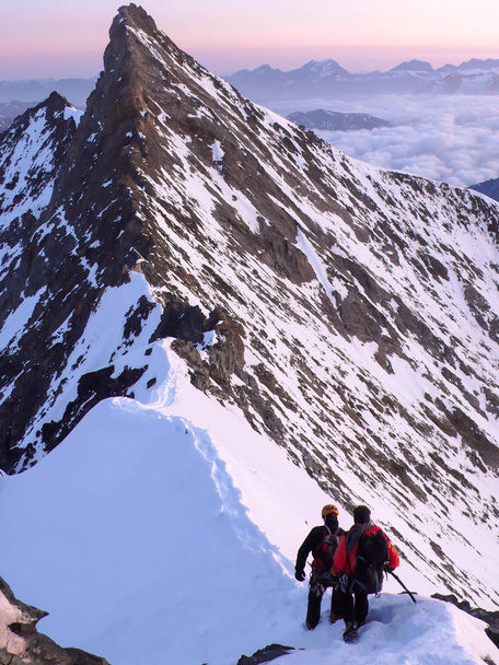guia de montanha e cliente em um cume de montanha estreito e exposto em direção a um alto cume ao nascer do sol
 - Foto, Imagem