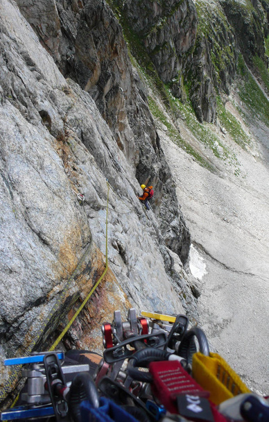 rock climber on a traditional old granite route in the Alps climbing while on belay from a guide above him with climbing equipment in the foreground - Photo, Image