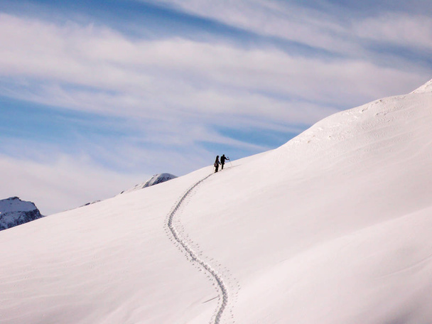 two backcountry skiers on a ski tour ascending a fresh powder snow slope in the Swiss Alps - Photo, Image