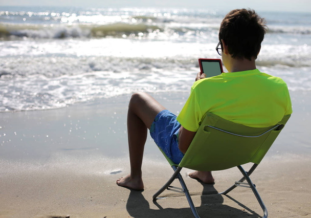молодий хлопчик з електронною книгою на березі моря влітку
 - Фото, зображення
