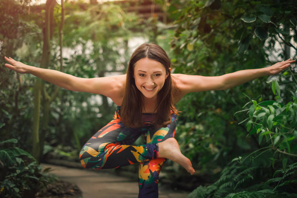 Mujer joven feliz haciendo ejercicios de yoga para el equilibrio en el invernadero
 - Foto, Imagen