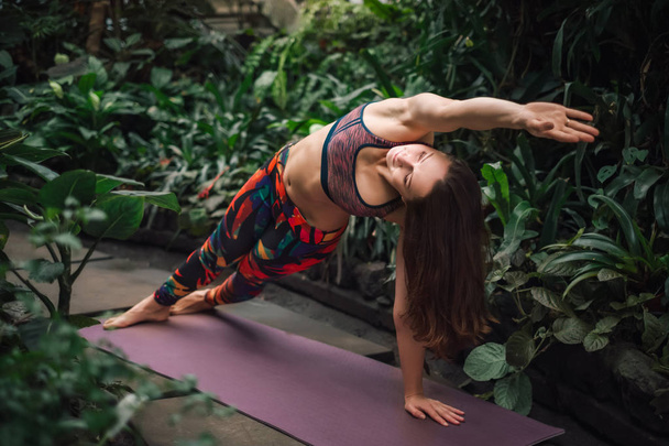 Atractiva instructora de yoga caucásica estirándose sobre una esterilla en el invernadero
 - Foto, Imagen