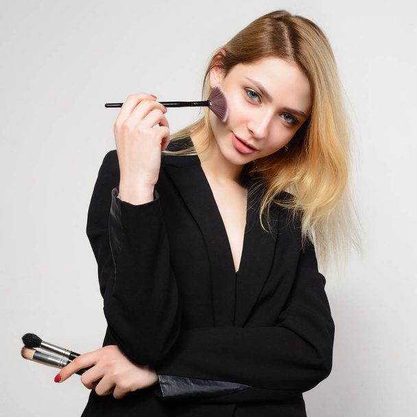Young blond woman in black jacket makes herself a make-up - Photo, Image