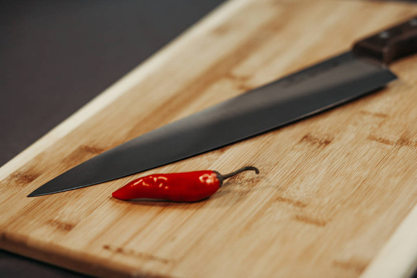 Red Chilli on the old wooden chopping board and shiny knife next to them - Foto, Imagem