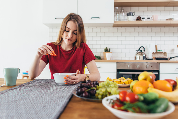 Young beautiful woman eating fruits and vegetables healthy food in kitchen. - Фото, изображение