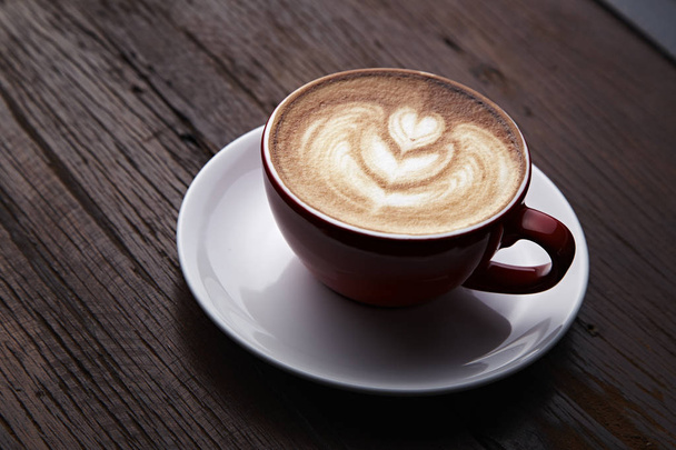 Rode kopje hete latte art koffie op houten tafel. Vintage kleurtoon - Foto, afbeelding
