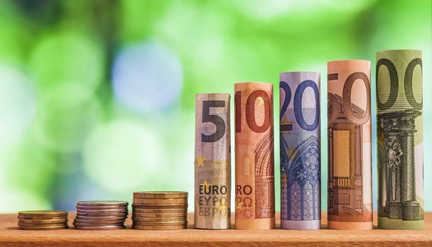 Five, ten, twenty, fifty and one hundred euro rolled bills banknotes, with euro coins on green blurred bokeh background. - Foto, Imagem