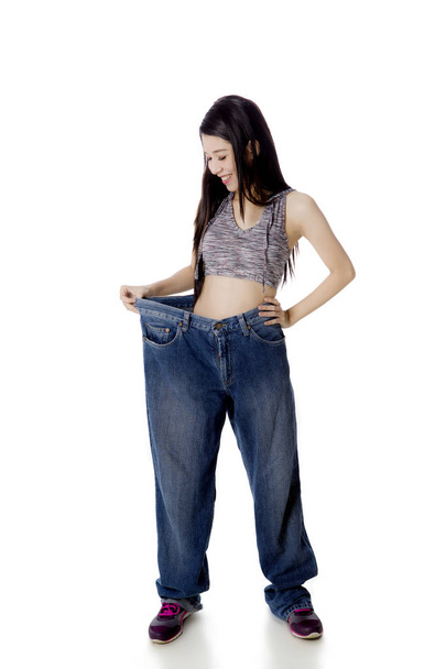Happy woman trying her old jeans on studio - 写真・画像