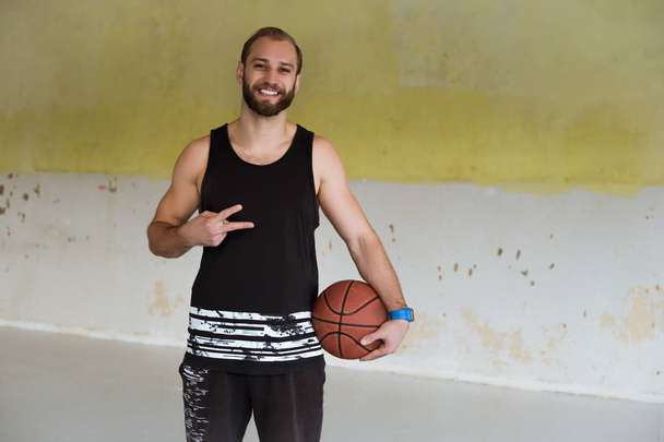 ein junger Basketballspieler lächelt und hält einen Ball in der Hand. - Foto, Bild
