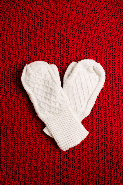 Πλεκτά γάντια σε κόκκινο φόντο πλεκτό. Χειμερινό ελάχιστο υπόβαθρο. Σύμβολο καρδιά επίπεδη lay, κορυφαία προβολή. - Φωτογραφία, εικόνα