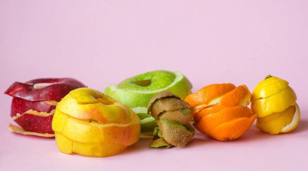 Kiwi, sinaasappel, citroen en rode, groene, gele appel schillen op roze achtergrond als een symbool van recycling circuleren economie - Foto, afbeelding