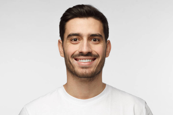 Close up portrait of smiling handsome man in white t-shirt isolated on grey background - Valokuva, kuva