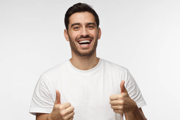 Young optimistic man isolated on grey background showing thumps up with positive emotions of content and happiness. Concept of satisfaction with quality and recommendation - Valokuva, kuva