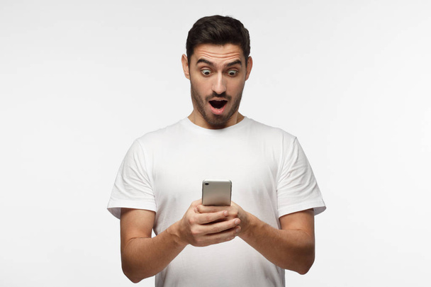 Portrait of young man isolated on gray background, looking agitated at display of her smartphone, impressed by media content from web - Foto, immagini