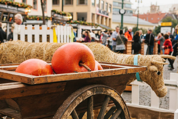 Celebrazione del raccolto autunnale. Mercato del traffico nella piazza della città con decorazioni. Una mucca di paglia e mele decorative in un carrello come un simbolo della vacanza
. - Foto, immagini