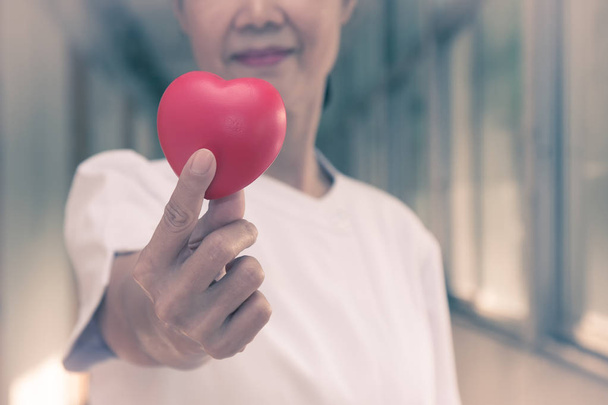 Enfermeira sênior segurando coração vermelho com amor para o dia dos namorados
 - Foto, Imagem