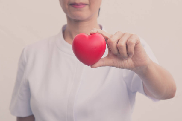 Enfermeira sênior segurando símbolo de coração vermelho em sua mão; isolar em branco
 - Foto, Imagem