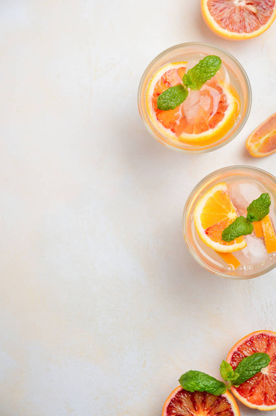 Холодный освежающий напиток с кровью апельсиновых ломтиков в стакане на белом бетонном фоне. Вид сверху, плоский, копировальное пространство
. - Фото, изображение