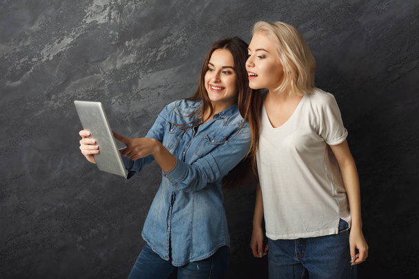 Curious female friends using tablet at dark studio background - Photo, Image