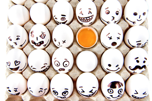 Eier mit gezeichneten Zeichentrickgesichtern und einem kaputten Ei in der Schale.  - Foto, Bild