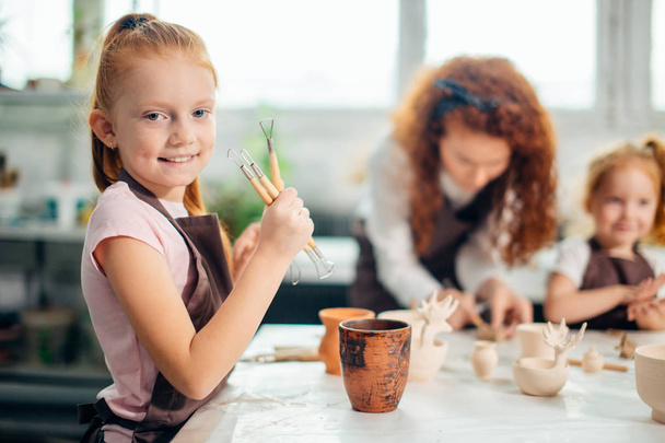 Girl stand near table and choose knife to work with clay - Photo, Image