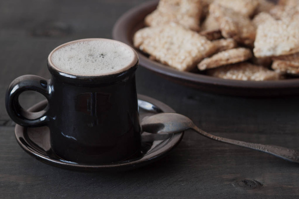 Em uma mesa de madeira é uma xícara de café e um prato com biscoitos
 - Foto, Imagem