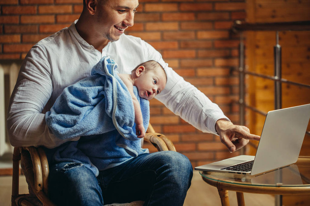 ο άνθρωπος που εργάζονται στο γραφείο στο σπίτι με το laptop, κρατώντας χαριτωμένο babys, κοιτάζει την οθόνη - Φωτογραφία, εικόνα