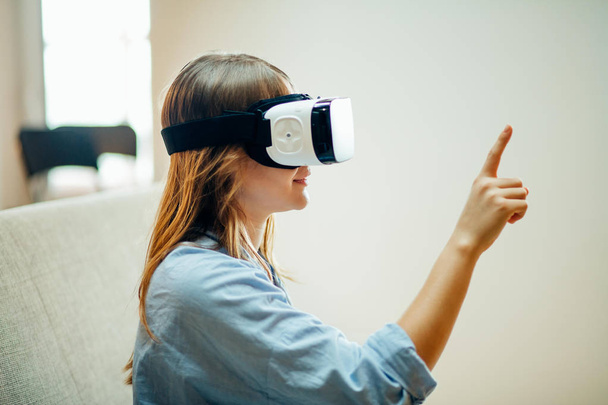 woman adjusting her VR headset and smiling while sitting on the carpet at home - Foto, imagen