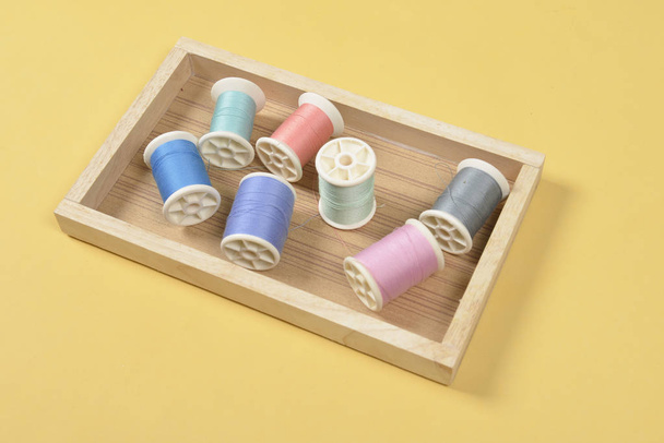 Flat lay of colored thread rolls for sewing on yellow background - Фото, изображение